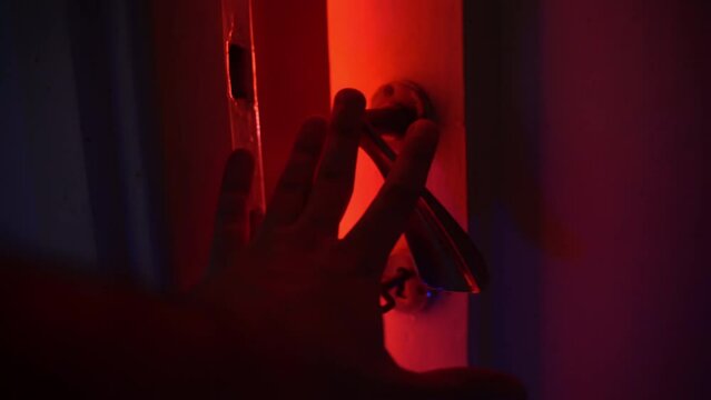 Horror scene with hand of murderer opening slowly door into the room with bright lighting, killer entering into dark room for attacking, burglar holding crime