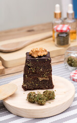 Chocolate cupcake muffins with cannabis buds in wooden spoon, oil pot and cooking jars. Marijuana hemp in food dessert. Chocolate herb muffins cooking. Marijuana cake on a brown wooden table.