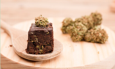 Chocolate cupcake muffins on wooden spoon with cannabis buds.Marijuana hemp in food dessert. Chocolate herb muffins cooking. Marijuana cake on a brown wooden table.