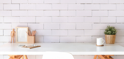 Stylish workplace with picture frame, coffee cup, potted plant and supplies on white table. Copy space.