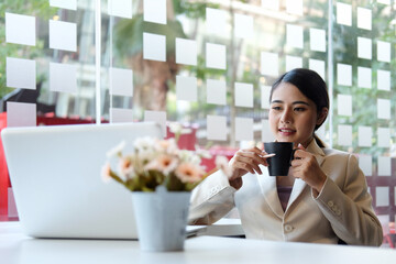 Relaxed businesswoman looking at laptop computer and drinking coffee.