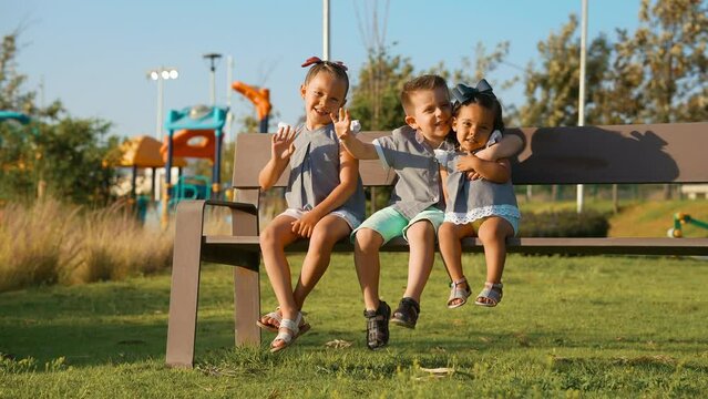 Ni&ntilde;os Felices amigos hermanos combinados vestidos igual amistad divertidos disfrutando sentados jugando en el parque en una banca al aire libre en juegos infantiles