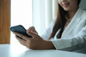 Cropped shot of cheerful businesswoman sitting at her office desk and using smart phone.