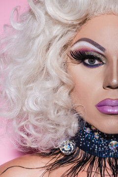 close up portrait of cropped drag queen with bright makeup looking at camera on pink.