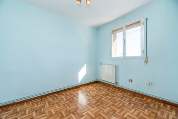Empty living room with wooden parquet flooring, blue painted walls and white aluminum radiator