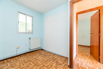 Empty room with wooden parquet, blue painted walls, aluminum window and mahogany colored woodwork