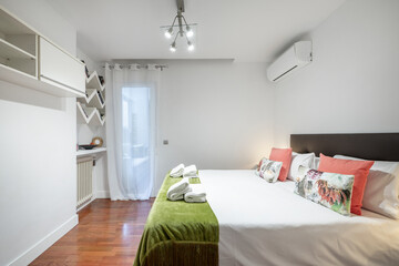 Bedroom with king size bed, shelves, cast iron radiator with cushions, matching side tables, black upholstered headboard, air conditioning, red parquet floor and green blanket