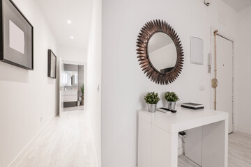 Hallway with a white wooden table with a toothed circular mirror and a hallway with light parquet floors