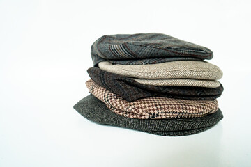 Stacks of classic hats like newsboy hats and flat hats in different colors and designs on a white background