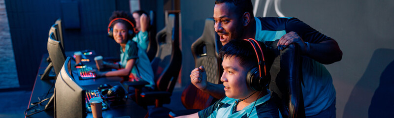 Side view of concentrated Asian male gamer supporting by teammate, winning while playing video...