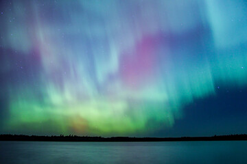 Northern lights erupt over remote Minnesota lake at night with rainbow of color shining off water Aurora Borealis nature show - obrazy, fototapety, plakaty
