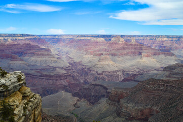 Hopi Point view of Grand. Canyon with red, gray, and yellow layered stone throughout the gorge under blue sky with few white clouds.