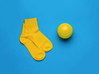 A big yellow tennis ball and yellow socks on a blue background. Flat lay.