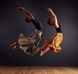 Synchronisity. Two contemporary dancers performing a synchronized leap in front of a dark background.