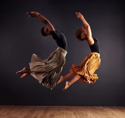Fotobehang Dansschool Synchronisity. Two contemporary dancers performing a synchronized leap in front of a dark background.