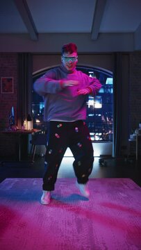 Vertical Screen: Portrait of a Handsome Young Man Dancing in Stylish Futuristic Neon Glowing Glasses, Having a Party at Home in Loft Apartment. Recording Funny Viral Videos for Social Media.