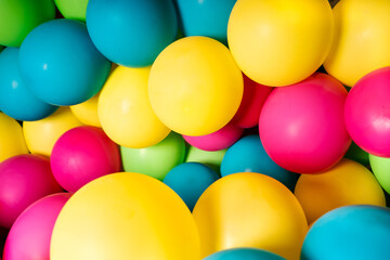 Colorful balloons all over the frame, lying one next to the other.  Many colored balloons looking like colored balls
