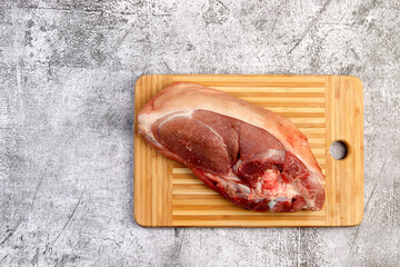 Raw pork shoulder on the skin with bone on a rectangular cutting wooden board on a dark grey background. Top view, flat lay