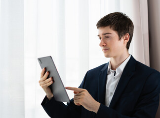 close up caucasian businessman happy working with tablet, wear suit, standing, looking at tablet, space at window light background. Young man work business with home office background and copy space