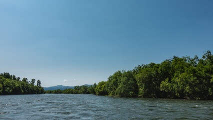 The blue River flows between banks overgrown with green vegetation. Ripples on the water. Mountains against the azure sky in the distance. Copy space. Kamchatka