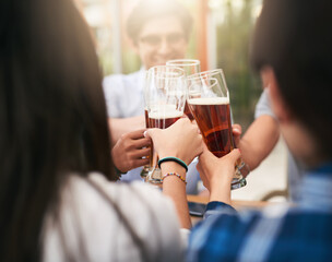 Whos buying the second round. Shot of a group of cheerful young business colleagues having a celebratory toast with beer around a table outside.