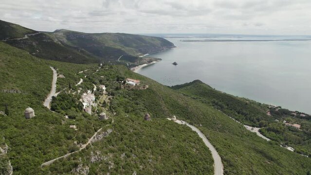 Winding road along Serra da Arrabida coastline reveals hillside convent; aerial
