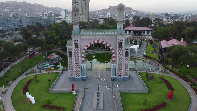 Drone 4k footage of a public park in Lima, Peru. Shot consists of flying through the top of an arch, in between two towers above. A lagoon can be seen and many green areas.
