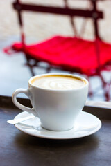 A white cup of cappuccino coffee on saucer on table on cafe, restaurant terrace.