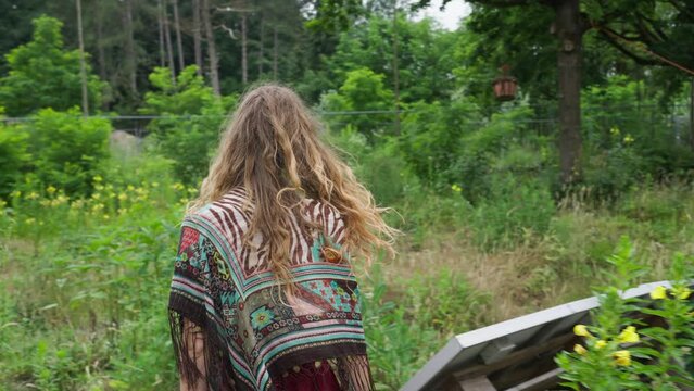 Free hippie young person walking back to camera through wild flowers field in nature, organic sustainable agriculture ecovillage tinyhouse lifestyle