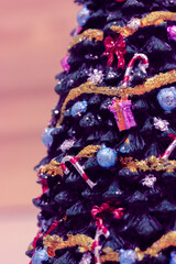 A beautifully decorated stylish ceramic Christmas tree decorated with different toys, garlands, lollipops, bows close-up at New Year's Eve 2022. Vertical photo. Trendy colors pink yellow violet toning