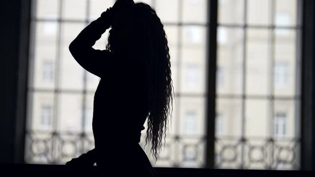 The silhouette of a long-haired woman in a room opposite a large window. Female depression and frustration