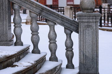 Balustrade of the rotunda under the snow. Gray granite exterior details during a snowfall. Fragment of a city landmark in winter.