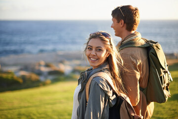 We go everywhere together. Portrait of a young couple standing on the edge of an embankment overlooking the ocean.