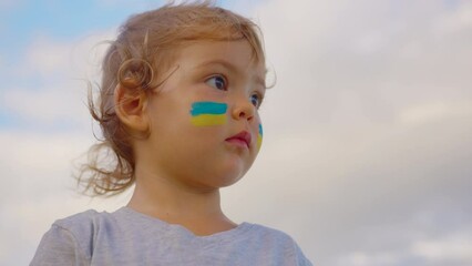 Close up portrait little baby with flag of Ukraine on face sitting alone. Protest against Russian war invasion in Ukraine. Ukrainian Flag, Protesters concept