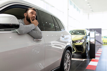 Fototapeta na wymiar a buyer in a car dealership sits in an SUV and thinks about buying and insuring a new car