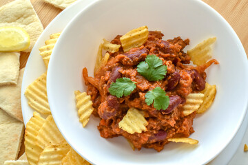 Chilli con carne with potato crisps in a white bowl. Traditional Mexican food.