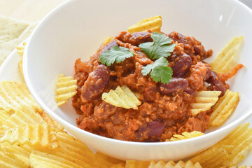 Chilli con carne with potato crisps in a white bowl. Traditional Mexican food.