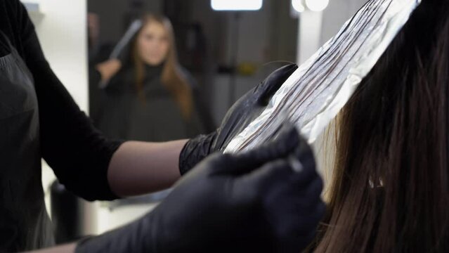 close-up side view of a strand of female hair on a special sheet of foil, the master applies hair dye with a brush. The process of highlighting by a professional master in a beauty salon. Life style