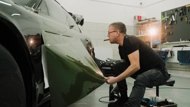 Close up shot of man vinyl wrapping the car door, pulling the film down. Process of vinyl wrapping a car using heat gun. Green vinyl film for car wrapping. High quality 4k footage