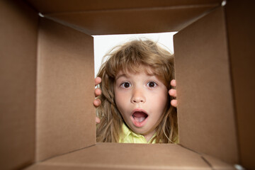 Happy little child boy is opening gift and looking inside cardboard box. Parcels, delivery service.