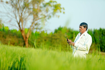 Indian farmer using smartphone at wheat field.