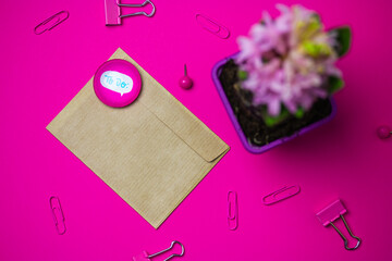 Brown envelope on pink background view from above. Stationery - pink paper binders, paper clips. Potted spring hyacinth flower in bloom on table Female desk with a letter, magnet stack with text TO DO
