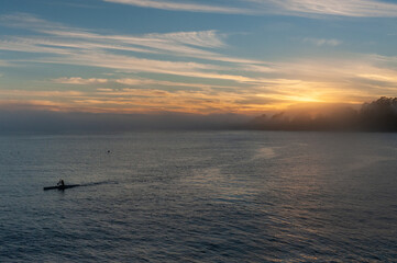 Fototapeta premium Silhoutte of a person in a kayak peddling in the Santa Cruz bay during sunset.
