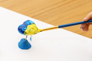 The child draw national flag of Ukraine painted yellow and blue on heart shape. The concept of patriotism, respect, support, help and solidarity with the citizens of Ukraine.