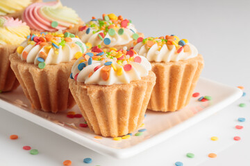 Close-up view of mini cupcakes decorated with candy sprinkles on white plate. Selective focus.