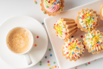 Top view of mini cupcakes decorated with candy sprinkles on white plate and cup of coffee.