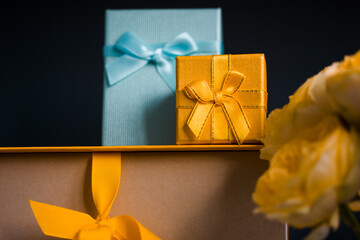 Yellow blue gift boxes stacked on dark black background, bouquet of yellow Austin roses. Greetings card with gifts, presents. Congratulations for birthday, Mother's Day, anniversary, Father's day.