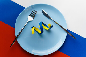 Blue and yellow ribbons as symbol of Ukraine on plate on Russian flag. Russia want to eat Ukraine