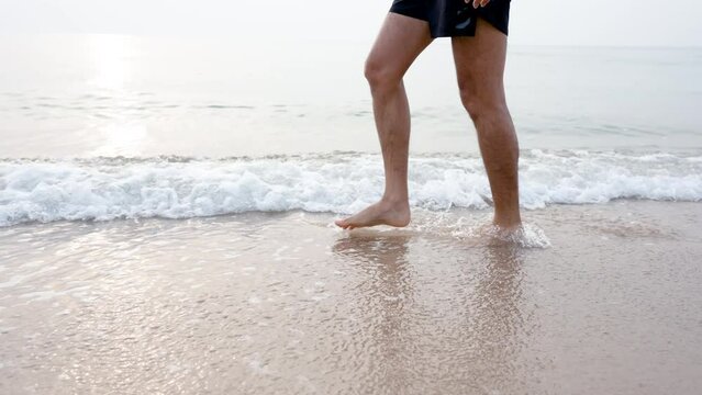 4K 50fps, Close-up of Asian men's feet, walks on the sandy beach in the morning when the weather is cool, and the cool, refreshing sea water hits the shore.