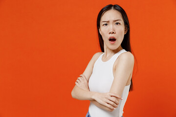Obraz premium Side profile view frowning shocked impressed surprised stupefied young woman of Asian ethnicity 20s years old in white tank top hold hands crossed isolated on plain orange background studio portrait.